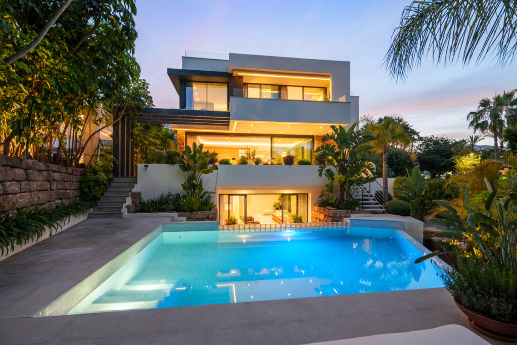 Belfry 1 – Estepona - modern three-storey luxury villa exterior with illuminated swimming pool at dusk, surrounded by tropical gardens