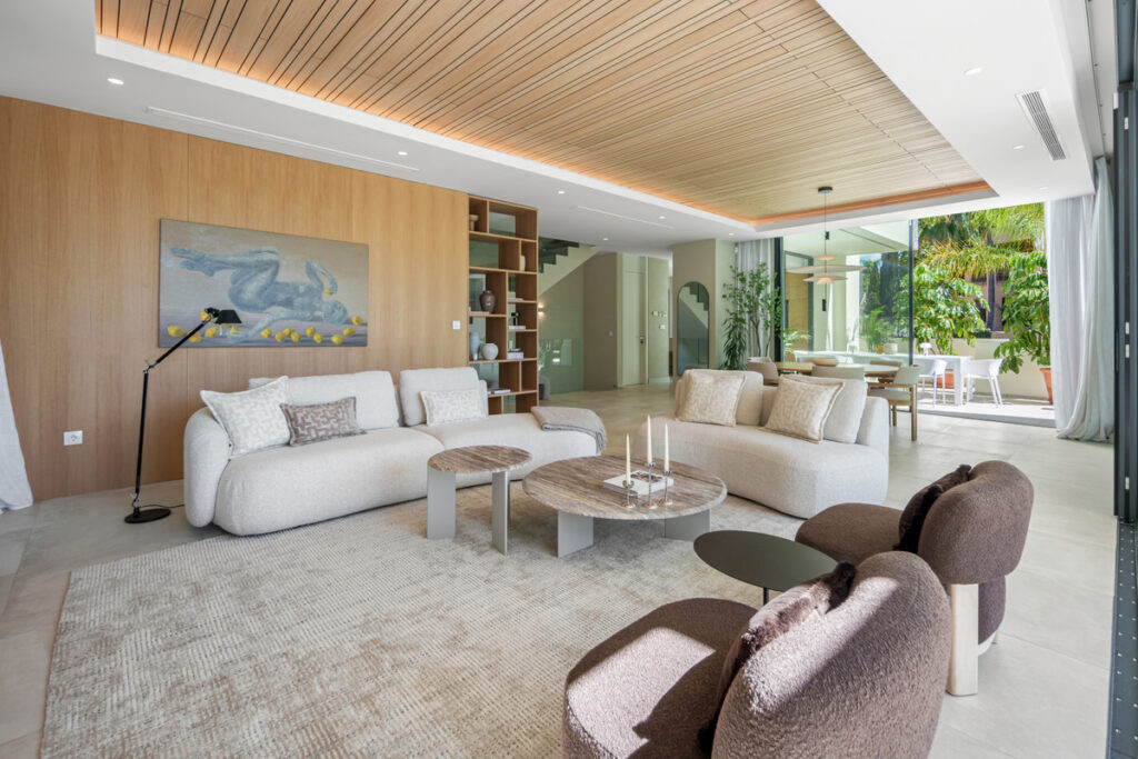 Belfry 1 – Estepona - open-plan living room with cream sofas, wood-panelled walls, and indoor-outdoor flow to garden terrace