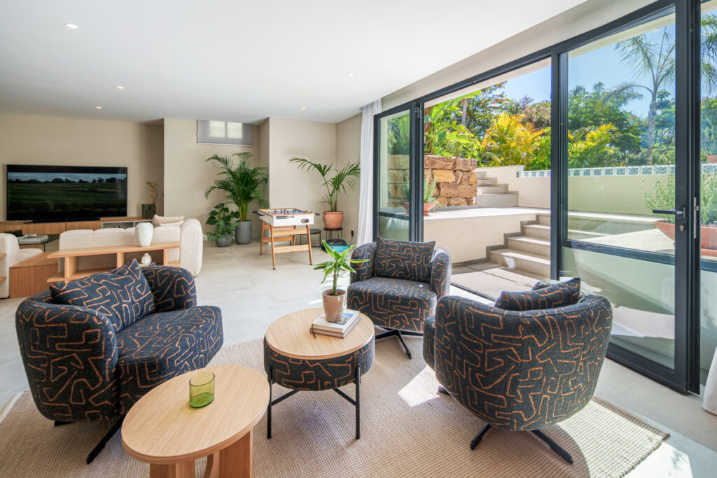 Belfry 1 – Estepona - open-plan living area with patterned armchairs, wooden coffee tables, large sliding glass doors and lush garden views