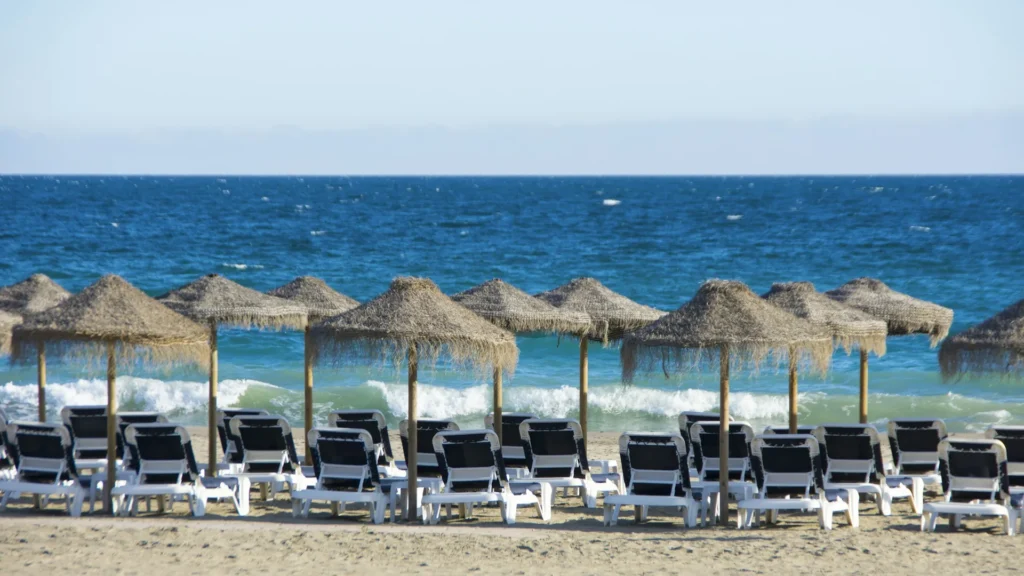 Straw parasols and sun loungers on a sandy Marbella beach with the Mediterranean behind, Costa del Sol