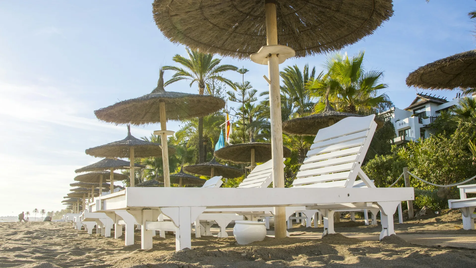 Sonnenliegen und Strohschirme an einem Sandstrand in Marbella an der Costa del Sol an einem sonnigen Tag